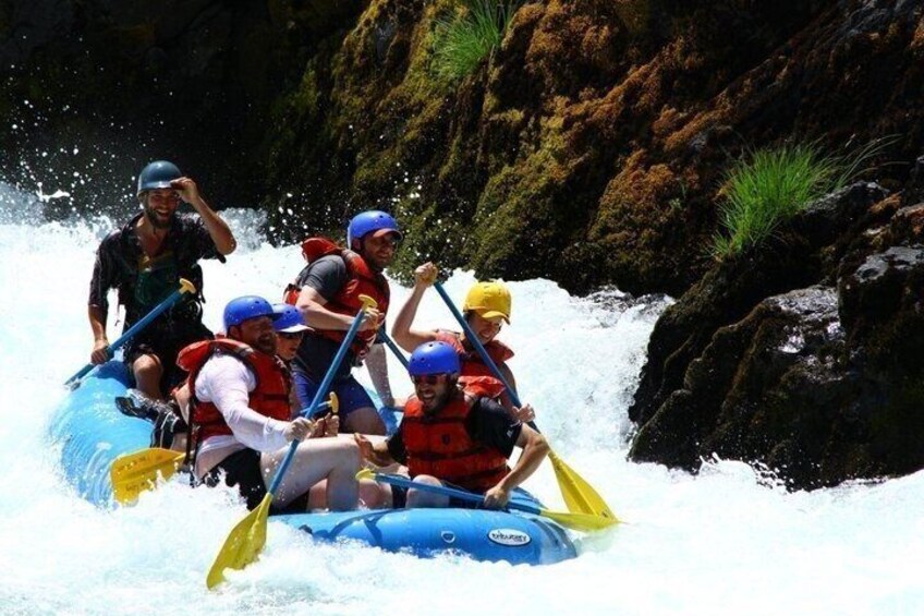 A group of people in a blue raft navigating a river with rapids. 1