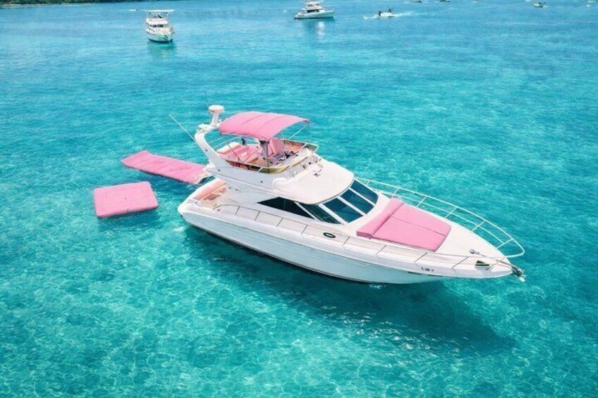 A white yacht with pink accents floating on clear turquoise water. 1