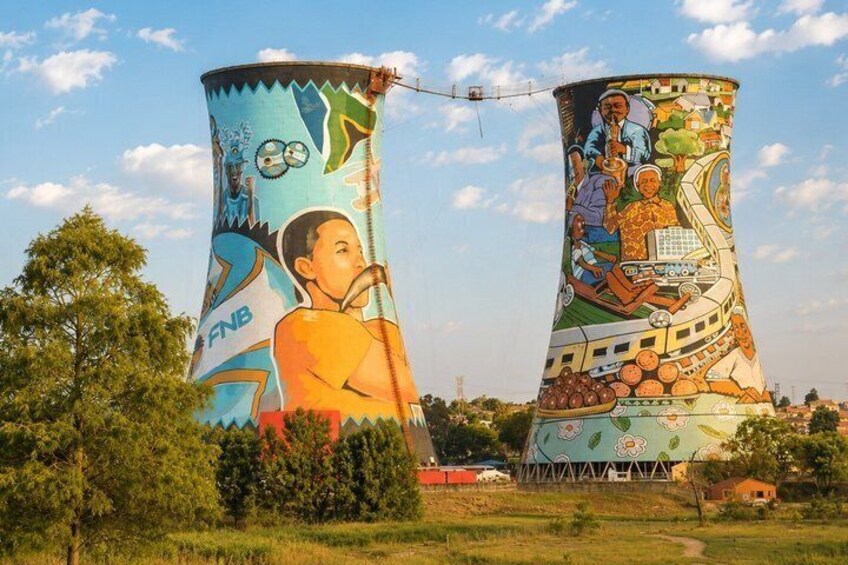 Two large cooling towers with colorful murals, surrounded by trees and a clear sky. 1