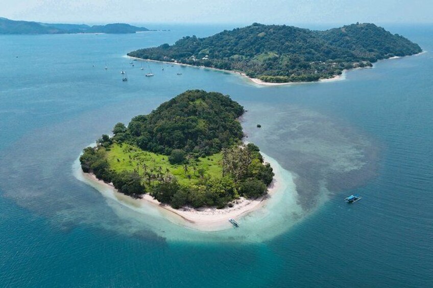An aerial view of a tropical island with a beach, surrounded by clear blue waters and a smaller island in the distance. 1