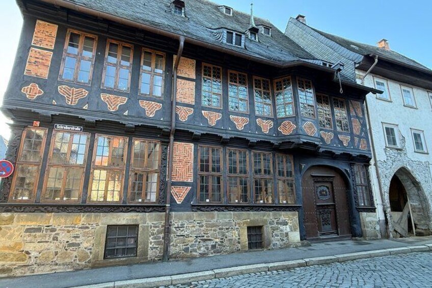 A half-timbered building with a stone base and a wooden upper story, featuring a large arched doorway and multiple windows. 4