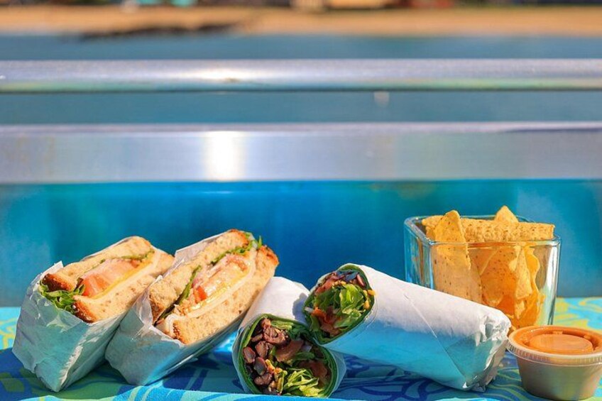 A poolside setting with sandwiches, chips, and a drink. 4
