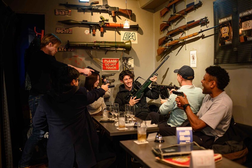 A group of people at a shooting range with various firearms displayed on the wall. 1
