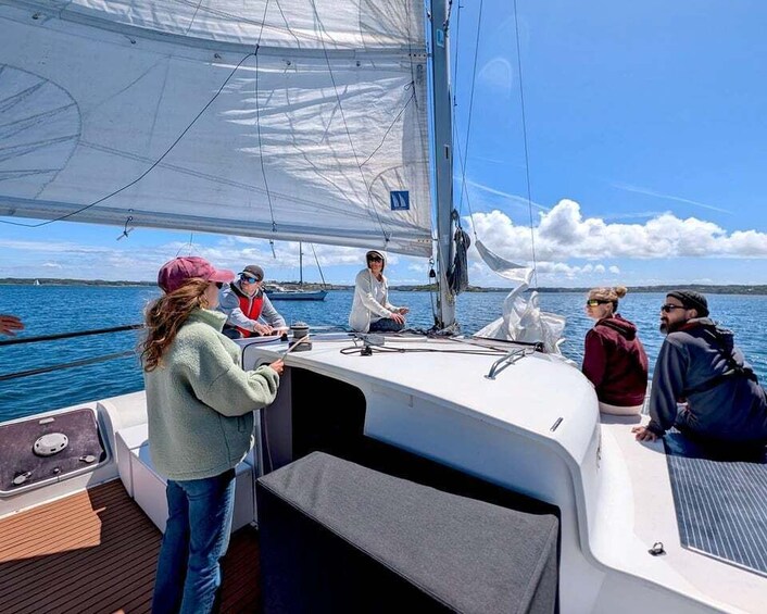 A sailboat with people on deck, a clear sky, and calm water. 1