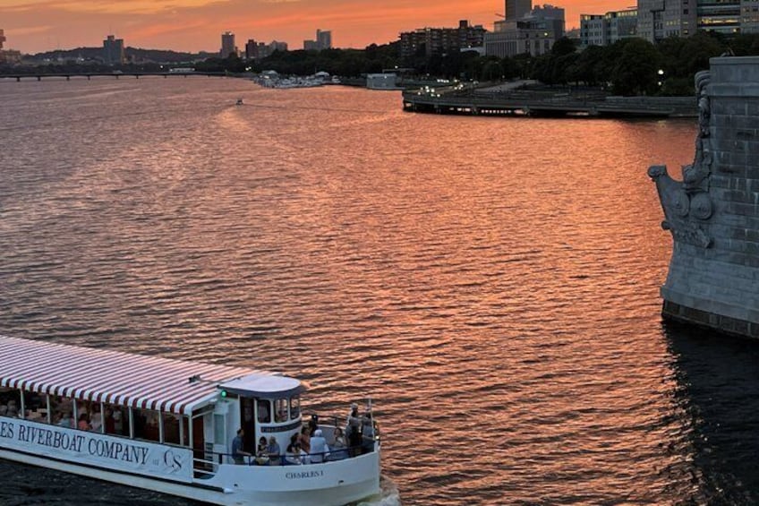 A riverboat with passengers, a sunset, and a city skyline in the background. 1