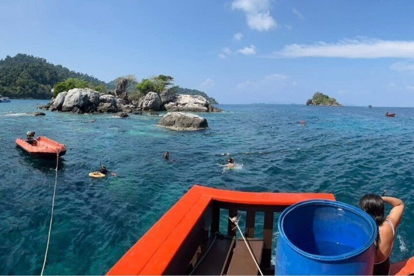 A boat with a red deck, clear blue water, and rocky islands in the distance. 5
