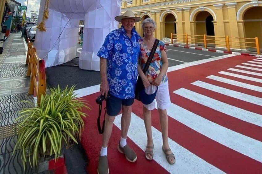A man and a woman standing on a red and white striped crosswalk with a yellow building in the background. 4