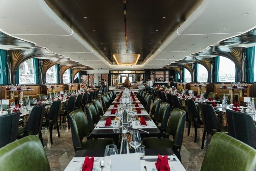 A long dining table with chairs, set for a meal, in a restaurant with large windows and a modern interior. 3