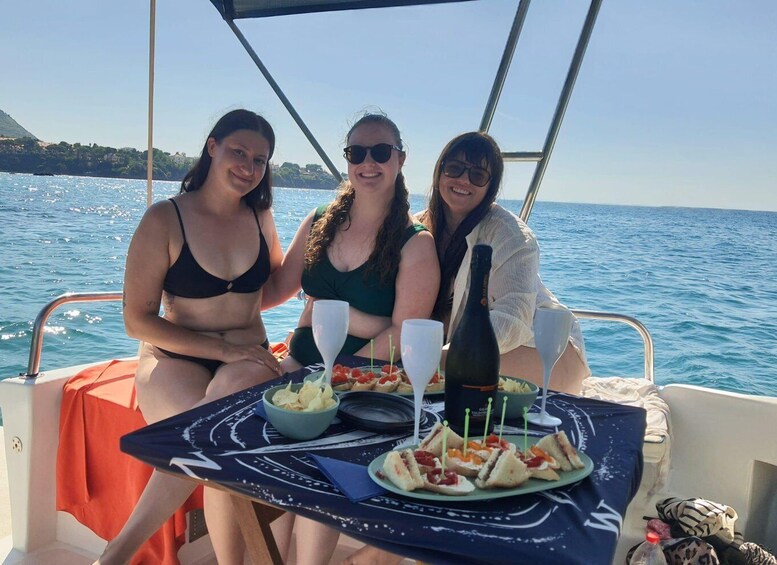Three people on a boat with a table set for a meal, glasses, and a bottle of wine. 4
