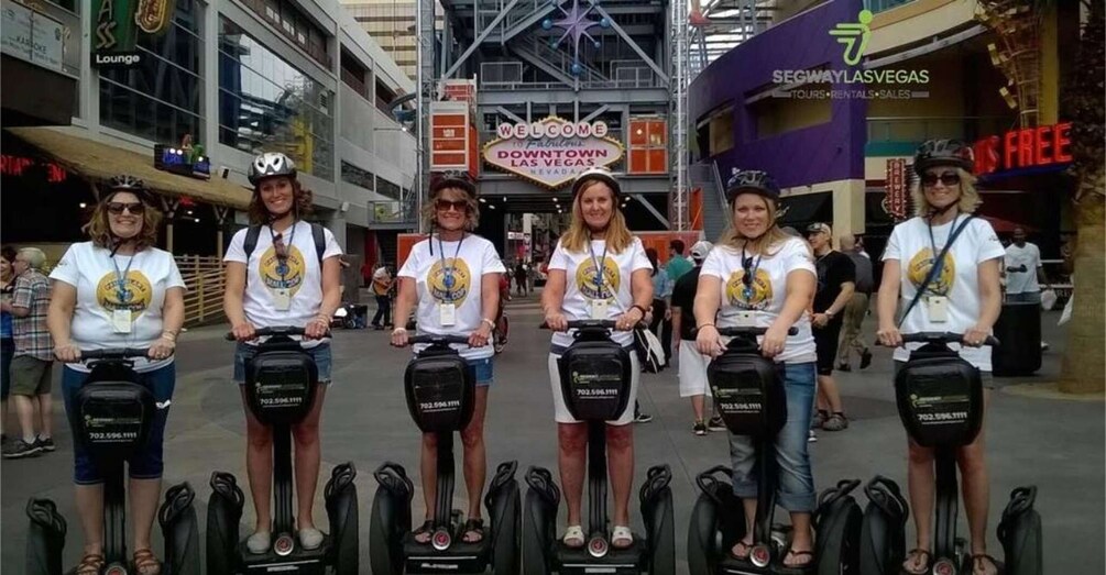 A group of people on electric scooters with a sign for Downtown Las Vegas in the background. 1