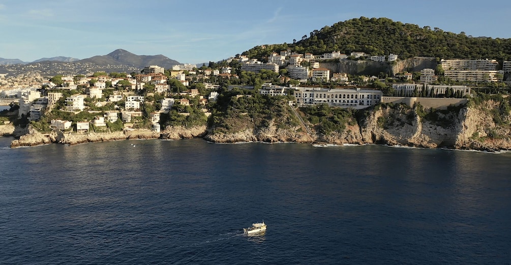 A coastal town with buildings on a hillside, a body of water, and a boat. 2