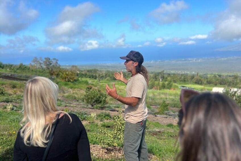 A person gesturing in a grassy field with a distant view of a coastline. 1