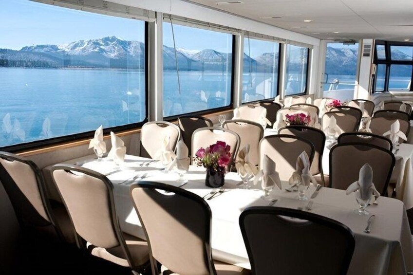 A dining area with tables set for service, large windows with a view of a lake and mountains. 2