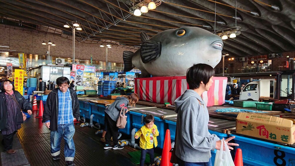 A market with a large fish sculpture, people shopping, and various stalls. 3