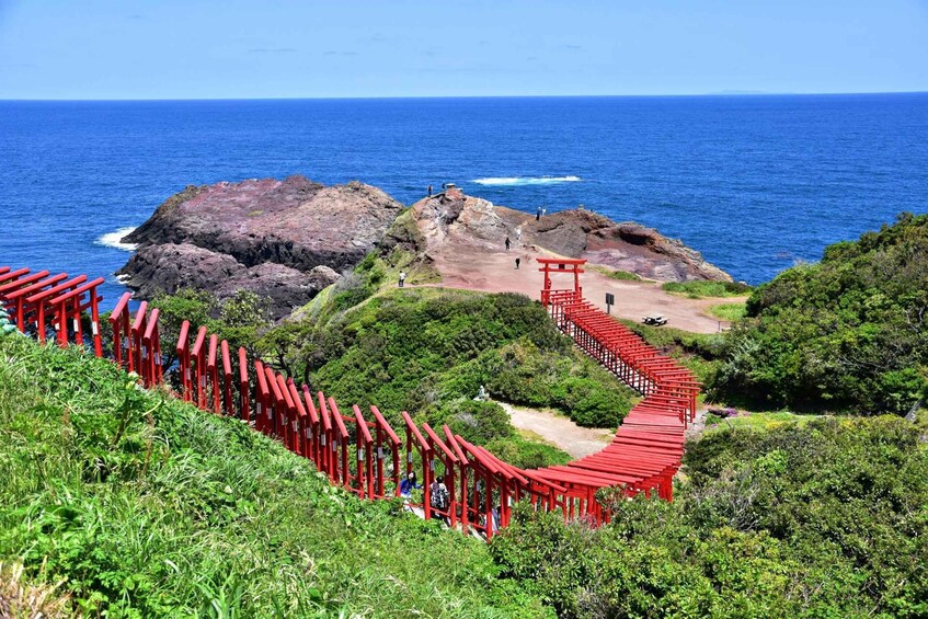 A red torii gate pathway leading to a rocky coastal area with the ocean in the background. 1