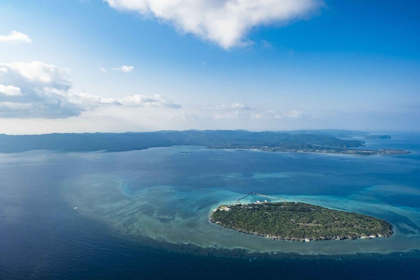 An aerial view of a tropical island surrounded by clear blue waters and a distant mountain range. 4