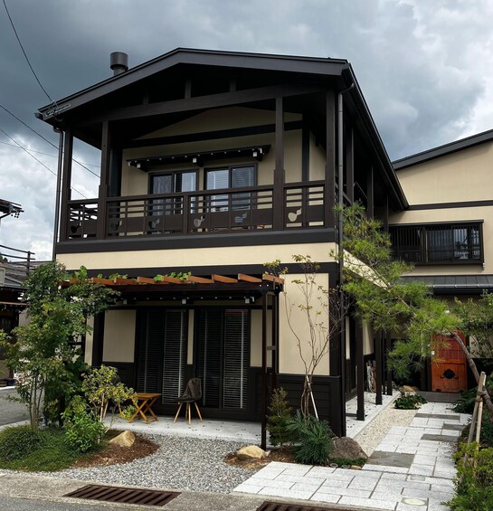 A two-story house with a balcony, surrounded by a garden with various plants and a gravel pathway. 3