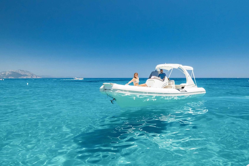 A small white boat with two people on a clear blue sea. 1