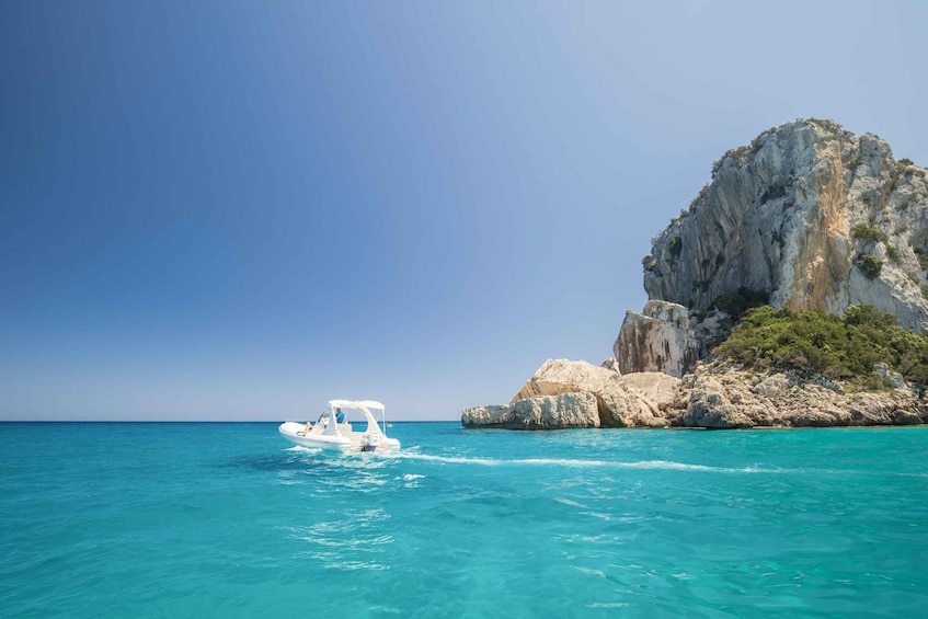 A white boat on turquoise sea, a rocky cliff, and clear blue sky. 2