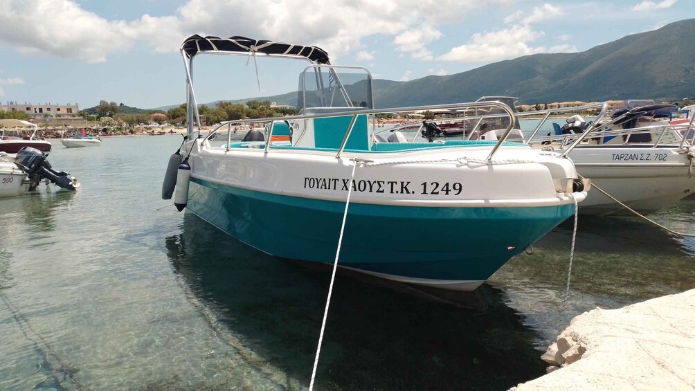 A boat named 'ΓΟΥΑΙΤ ΧΑΟΥΕ Τ.Κ. 1249' docked at a marina with other boats, clear water, and mountains in the background. 2