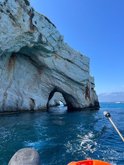 A boat near a rock formation with a natural arch over the water. 4