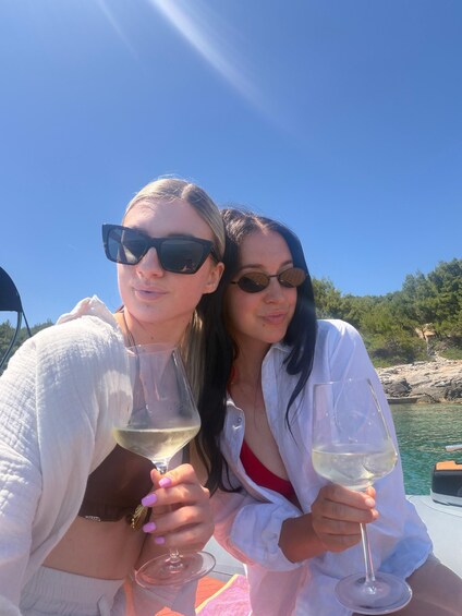 Two people on a boat with drinks, clear skies, and a rocky shoreline in the background. 5