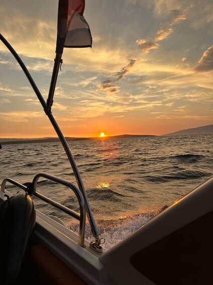 A sunset over the ocean with a boat's railing and a flag in the foreground. 3