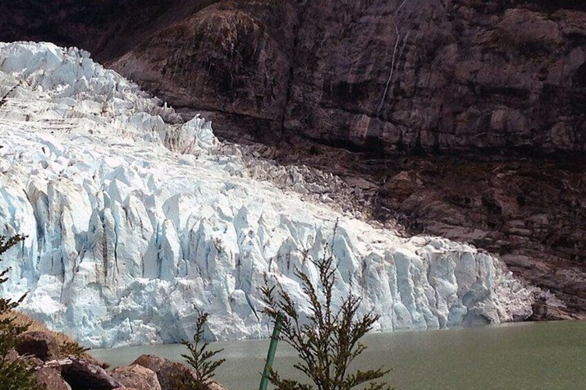 A glacier with a body of water in the foreground and rocky cliffs in the background. 1