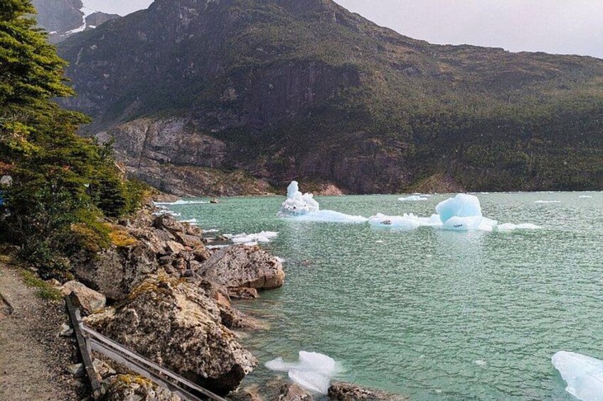 A coastal landscape with icebergs, rocky shore, and a mountain in the background. 2