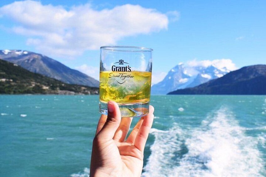 A hand holding a glass of beer with a mountain and lake in the background. 2