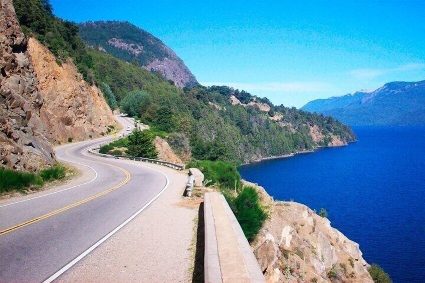 A winding coastal road with a guardrail, surrounded by rocky cliffs and dense greenery. 2