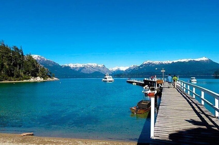 A pier extending into a calm lake with boats docked, surrounded by snow-capped mountains. 4