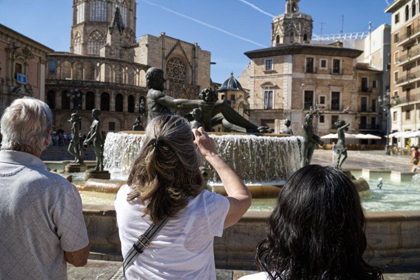 A group of people observing a fountain with statues in an urban square. 2