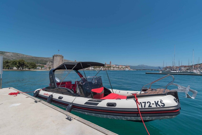 A small motorboat docked at a pier with a clear blue sky and a distant view of a town and hills. 2