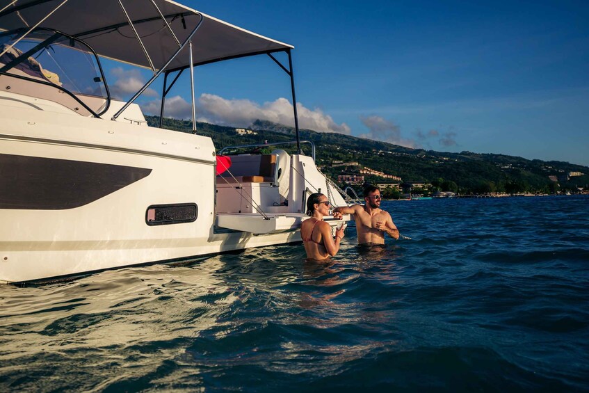 A white yacht with a canopy, two people in the water, and a coastal town in the background. 4