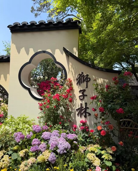 A sign with Chinese characters, surrounded by a variety of flowers and greenery. 1