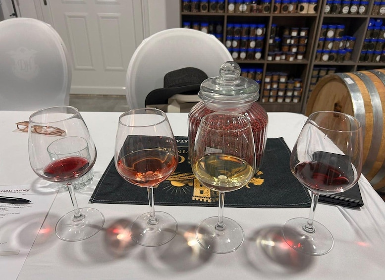 A tasting table with four wine glasses, a glass jar, and a wooden barrel in the background. 5