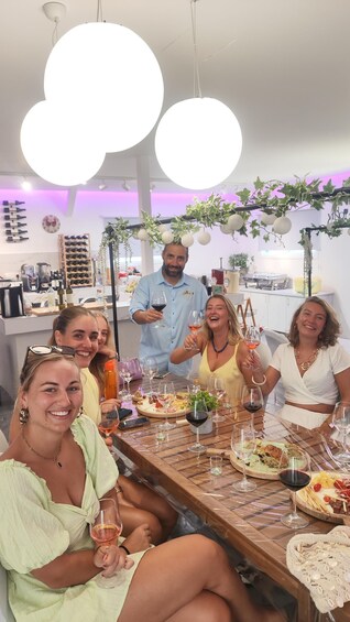A group of people toasting with wine glasses at a dinner table in a modern kitchen with pendant lights and a wine rack. 1