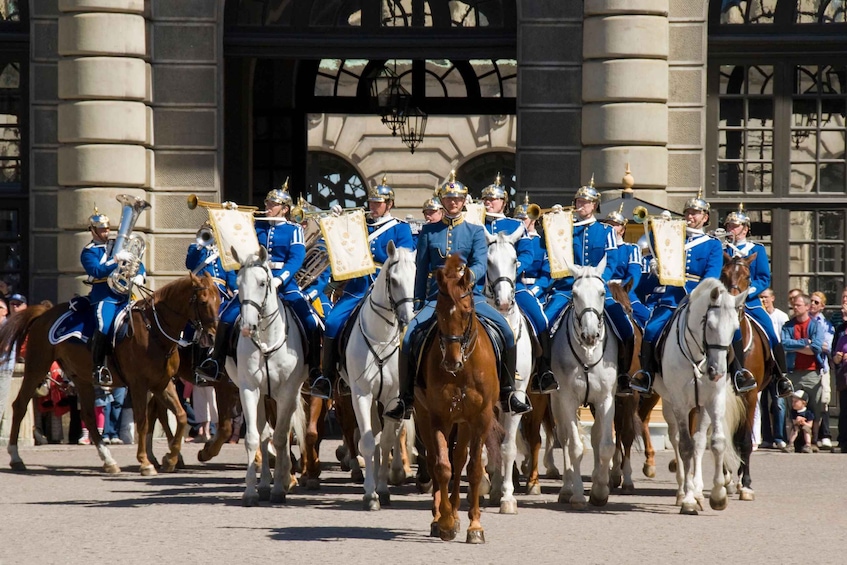 A group of uniformed guards on horseback in formation, with a building in the background. 1