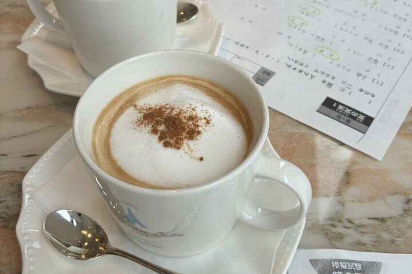 A cup of coffee with a frothy top and a sprinkle of cinnamon on a saucer, accompanied by a spoon and a menu. 5