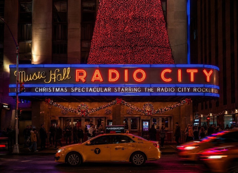 A building with a large red Christmas tree and neon signs for 'Music Hall RADIO CITY' and 'Christmas Spectacular.' 2