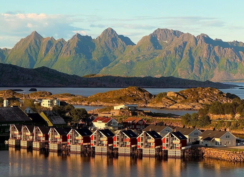A coastal village with red houses on stilts, a calm sea, and mountains in the background. 1