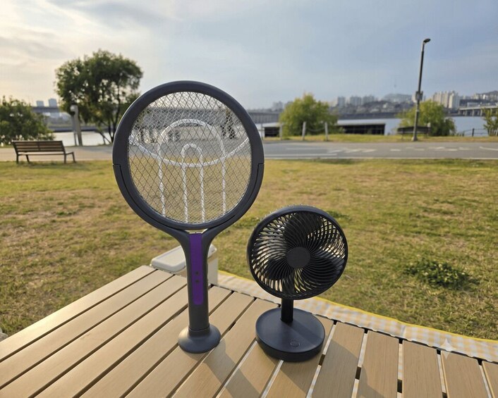 A tennis racket and a portable fan on a wooden table in an outdoor setting. 2
