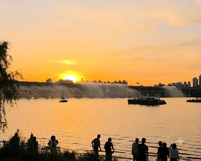 A sunset over a river with a waterfall, boats, and people by the water. 3