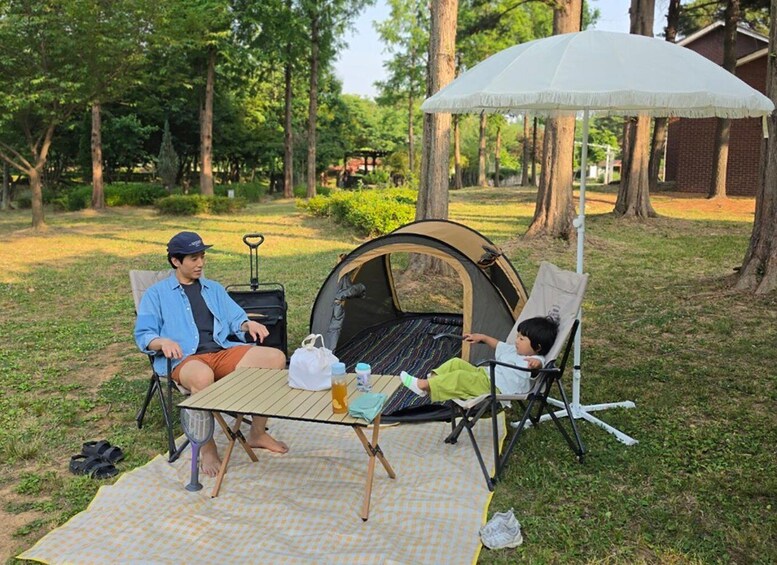 A camping setup with a tent, a table, and two chairs in a grassy park. 1