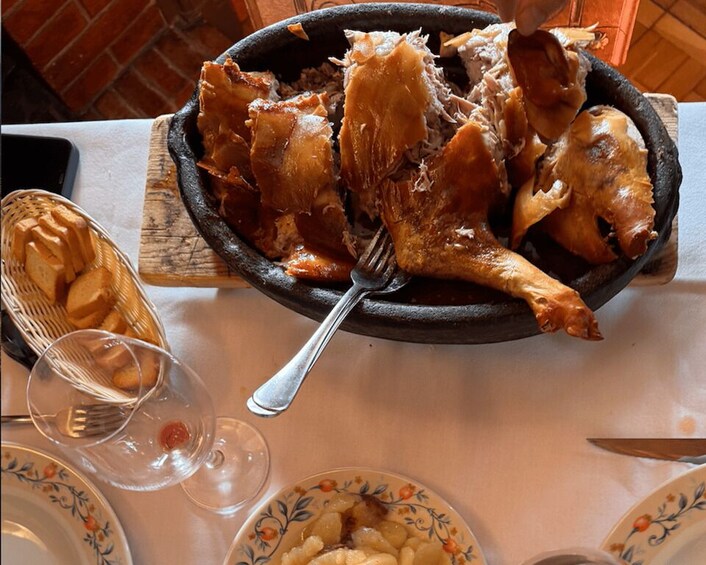 A roasted chicken on a plate with a fork, surrounded by bread and wine glasses. 3