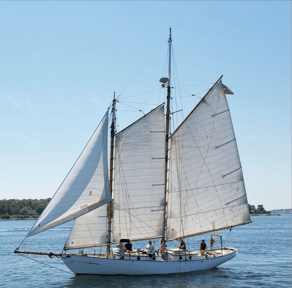 A sailboat with two masts and sails, on calm water with a clear sky. 1