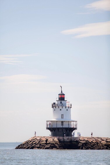 A lighthouse on a rocky outcrop with people standing around it. 3