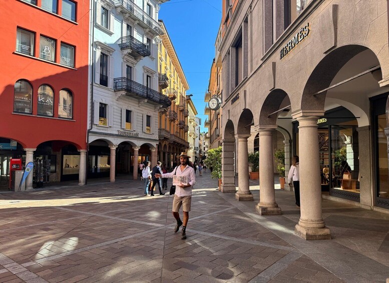 A pedestrian street lined with shops and buildings, including a visible storefront with the name 'Hermes.' 1