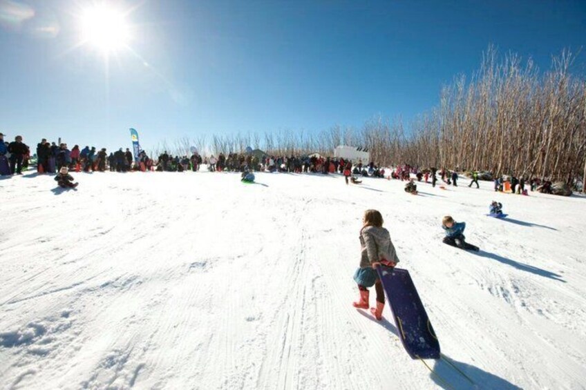 A snowy landscape with people sledding and a clear blue sky. 3